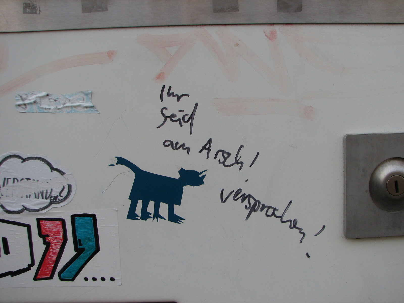 Wandoberfläche mit verschiedenen Graffiti-Elementen: ein dunkelblau gezeichneter Katzenkopf im Profil, handgeschriebener Text daneben, weitere Tags und farbige geometrische Formen in Rot und Blau sowie rosa Farbspritzer.