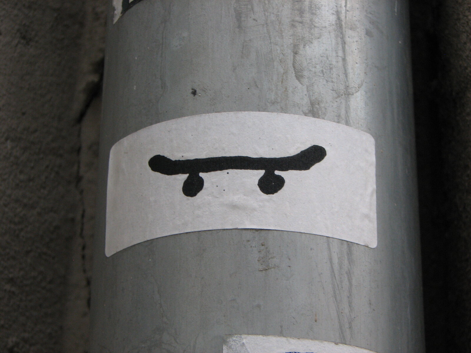 Weißer Sticker mit schwarzer Zeichnung eines Skateboards auf grauem Untergrund. Das Motiv zeigt ein einfaches, stilisiertes Skateboard mit vier Rädern.