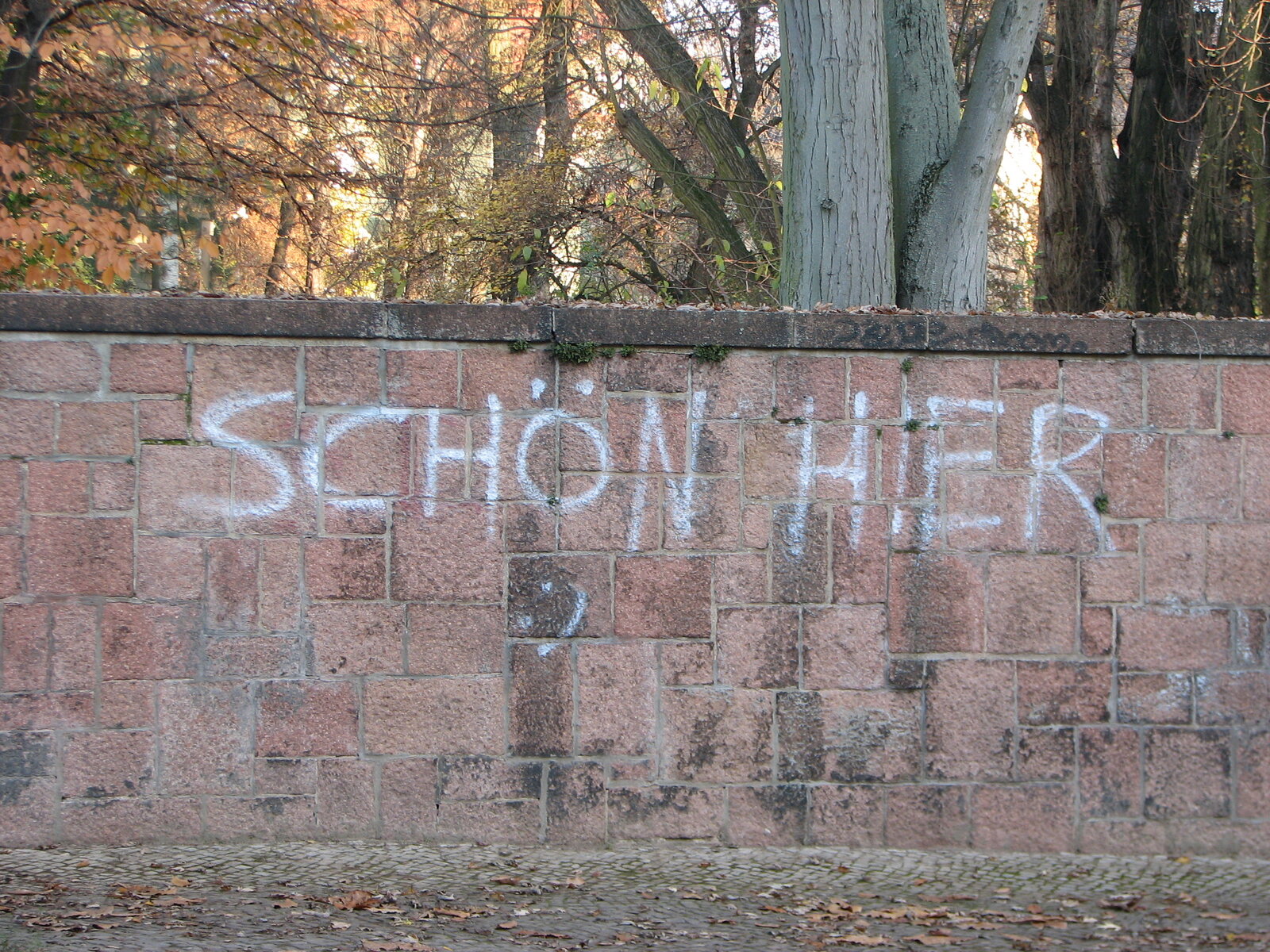 Weißes Graffiti-Schriftzug "schön hier" auf einer roten Backsteinmauer. Darunter ein einfacher Smiley.