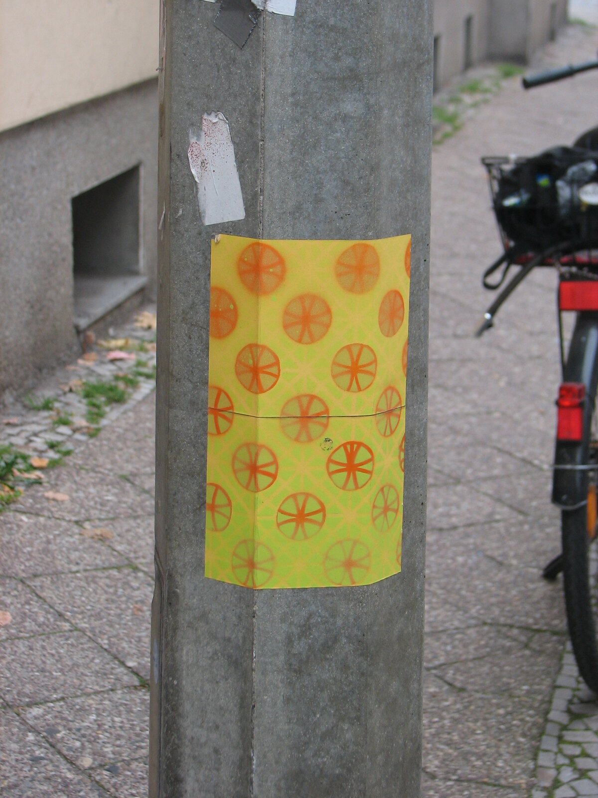 Ein gelber rechteckiger Sticker auf einem grauen Betonsockel zeigt ein Muster aus orangen Kreisen mit gekreuztem Muster.