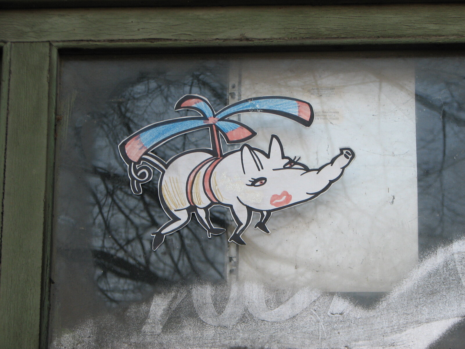Ein aufgeklebter Sticker zeigt ein weißes Schwein in Seitenansicht mit blauen und roten Bändern oder Flügeln. Das Motiv ist schwarz konturiert und farbig ausgefüllt, aufgebracht auf einer hellen Wandfläche mit Graffiti-Hintergrund.
