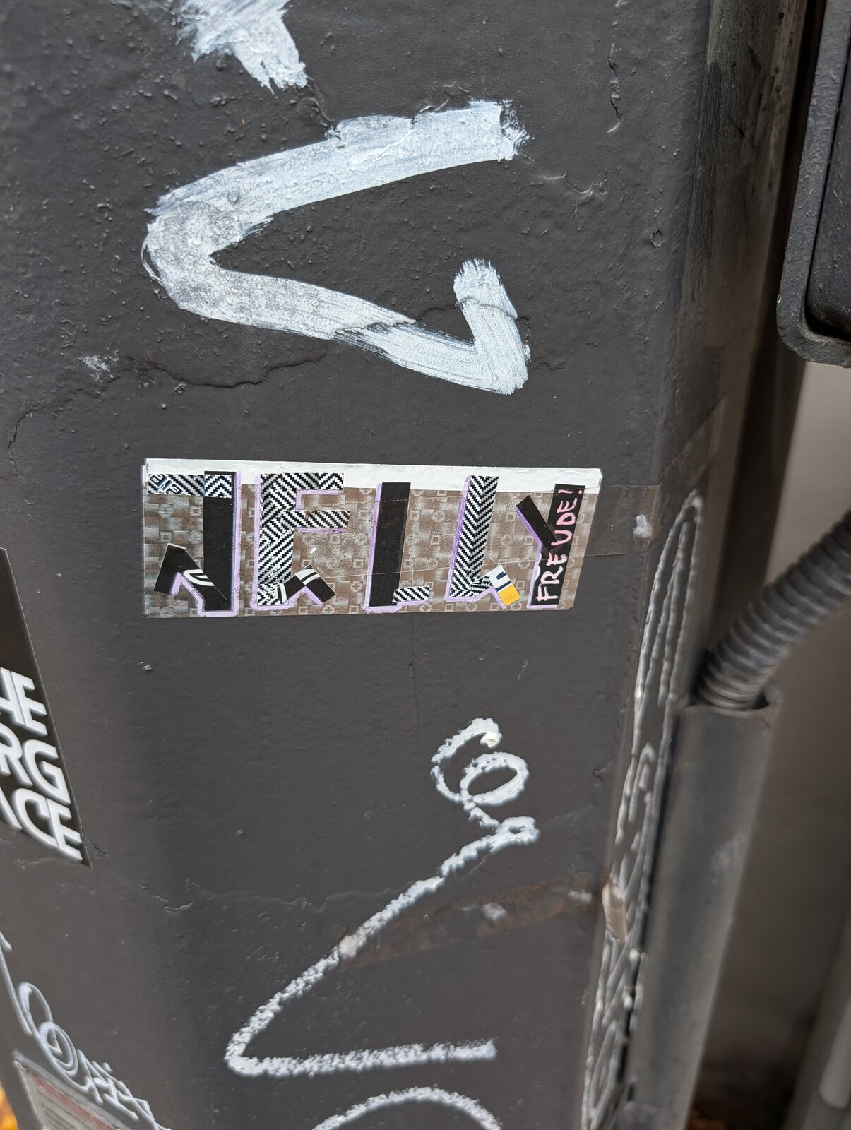 Auf grauem Untergrund ein weißes Pfeil-Symbol nach links, darunter ein bunte Sticker-Komposition mit geometrischen Mustern und Schriftzügen in Schwarz-Weiß, sowie weiße Linienzeichnungen. Zu erkennen ist das Wort Jelly, ganz rechts Freude.