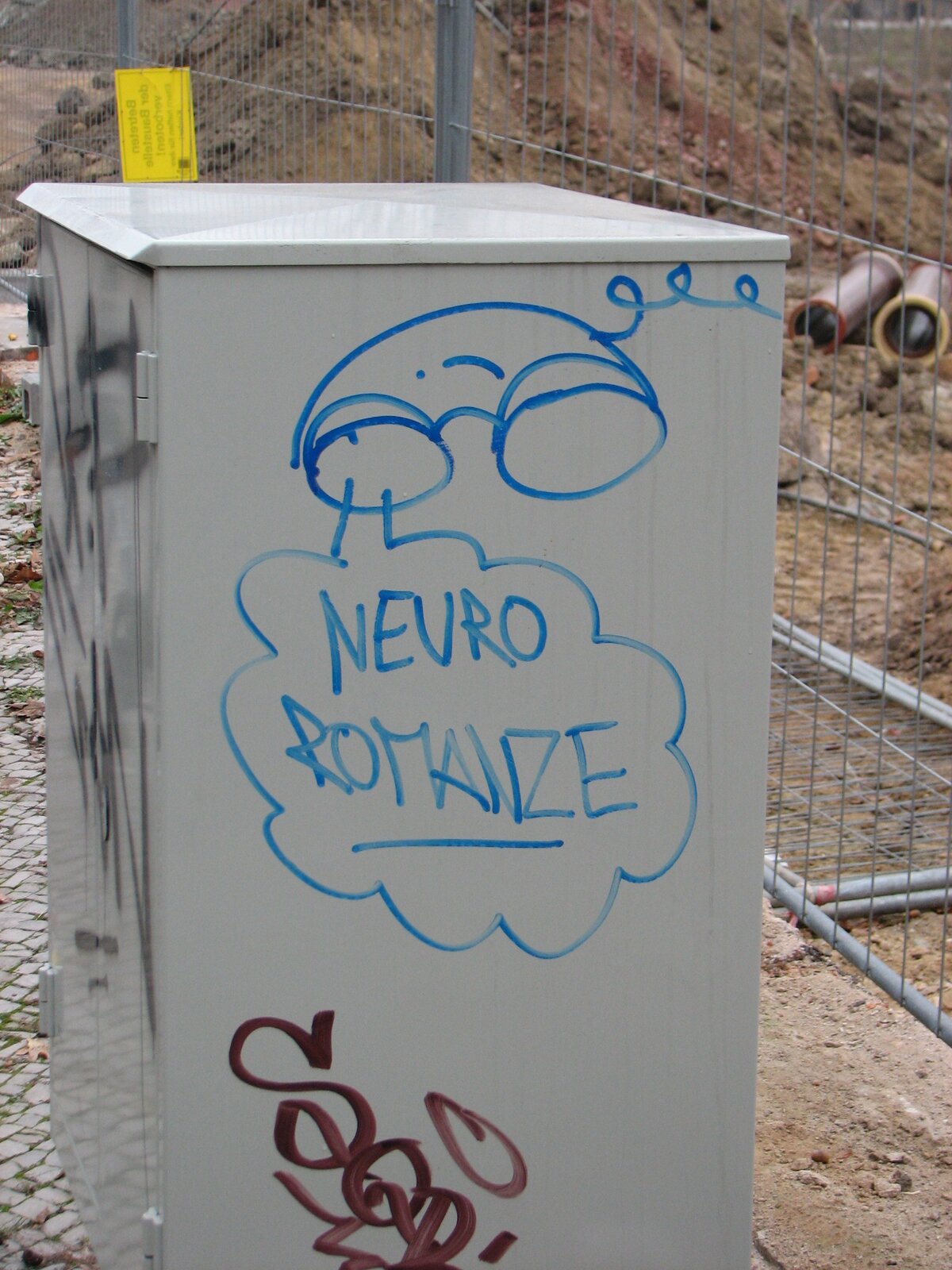Hellgrauer Stromkasten mit blauer Marker-Zeichnung: ein Telefonhörer mit dem Schriftzug NEURO ROMANZE. Unten rotbraune Schrift.