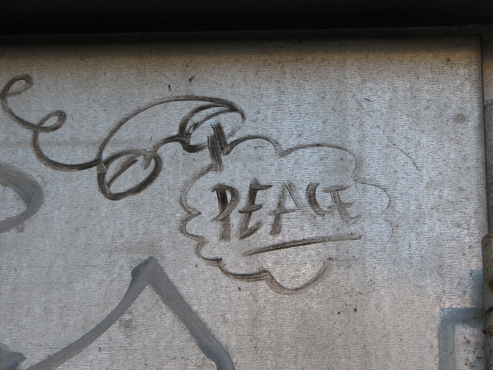 Schwarze Schrift auf einer grauen, leicht strukturierten Metalloberfläche: das Wort PEACE in einer wolkenförmigen Umrandung, daneben ein alter Telefonhörer.