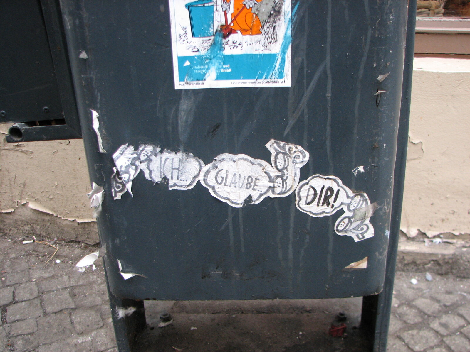 Schwarze Mülltonne mit weißen handschriftlichen Sticker-Tags. In der Mitte sind drei Telefonhörer zu erkennen, an jedem hängt eine Sprechblase. Darin stehen die Worte "ich", "glaube" und "dir".